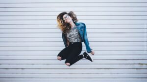 junge Frau im Sprung vor grauer Wand
