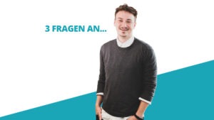 Junger Mann steht lachend vor blau-weißem Hintergrund