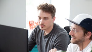 Zwei Männer sitzen vor einem PC und arbeiten