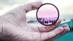 Hand im Vordergrund hält Vergrößerungsglas, mit dem man auf das Meer blicken kann