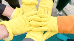 Sechs Hände mit gelben Handschuhen berühren sich in der Mitte zum Gruß