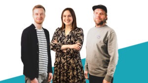 Drei Personen, links und rechts ein Mann und in der Mitte eine Frau, vor einem weißen Hintergrund, lächeln in die Kamera