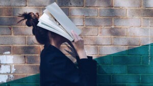 Frau mit braunen Haaren, von der Seite zu sehen, hält sich ein Buch ins Gesicht