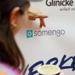 Frau zeigt mir ihren Fingern auf das Somengo-Logo einer Sponsoring-Wand