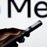 Hand mit Smartphone in der Hand und im Hintergrund Meta Logo