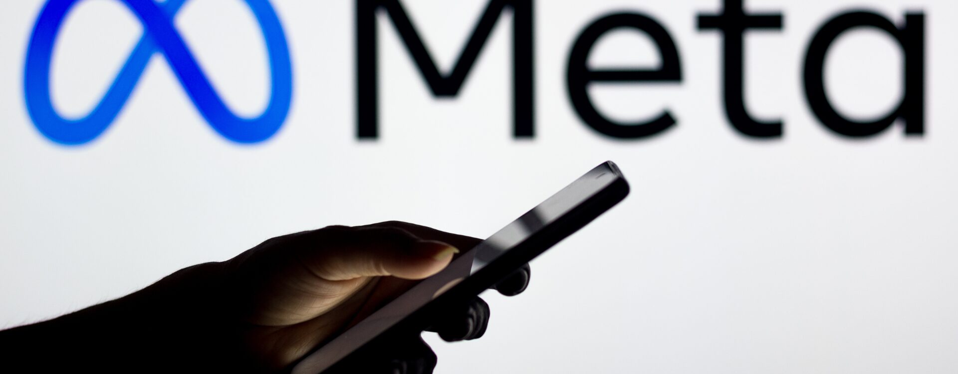 Hand mit Smartphone in der Hand und im Hintergrund Meta Logo
