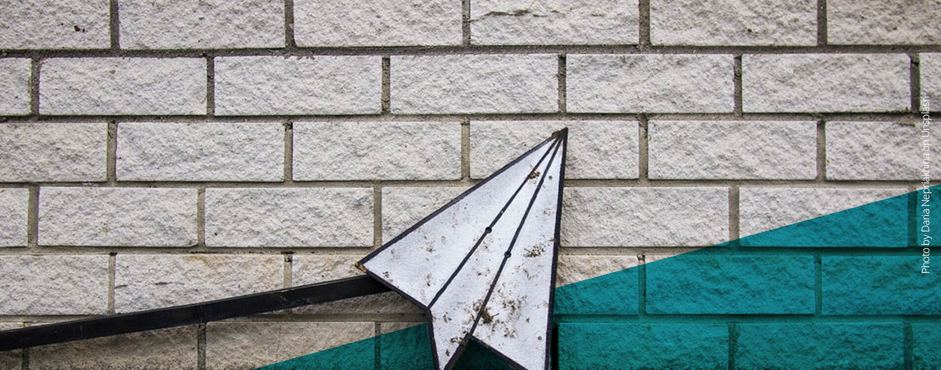 Papierflugzeug aus Eisen vor einer Steinmauer