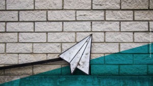 Papierflugzeug aus Eisen vor einer Steinmauer