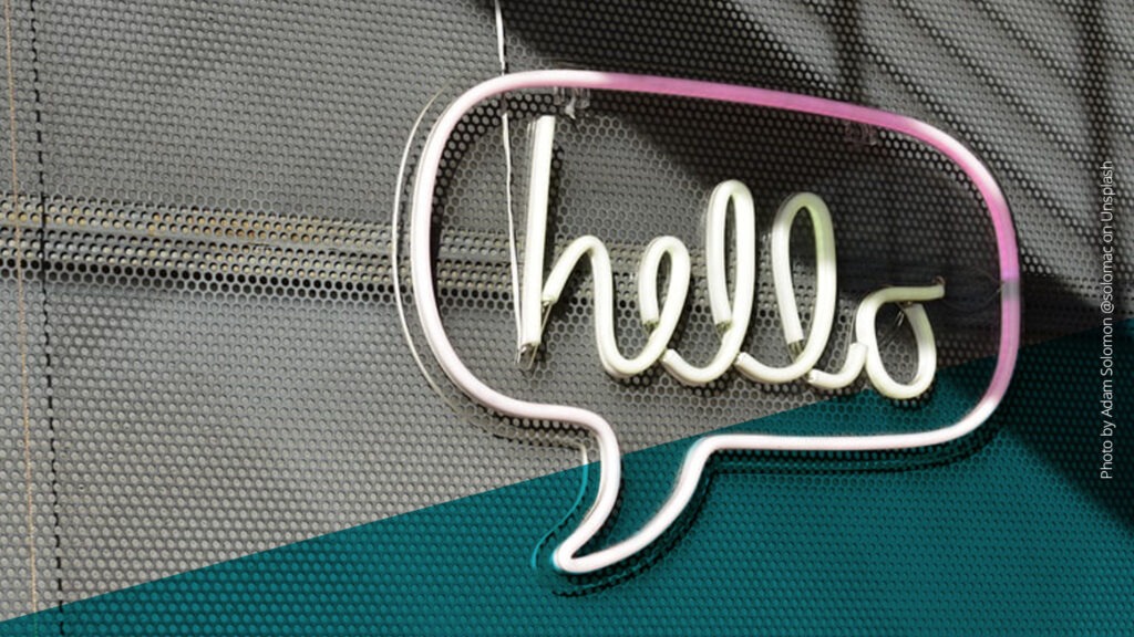 Sprechblase mit Schriftzug "hello" aus Leuchtröhren an einer Wand