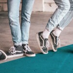 Vier Beine nebeneinander, alle tragen helle Jeans und schwarzweiße Schuhe