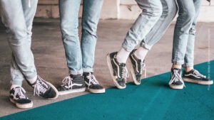Vier Beine nebeneinander, alle tragen helle Jeans und schwarzweiße Schuhe
