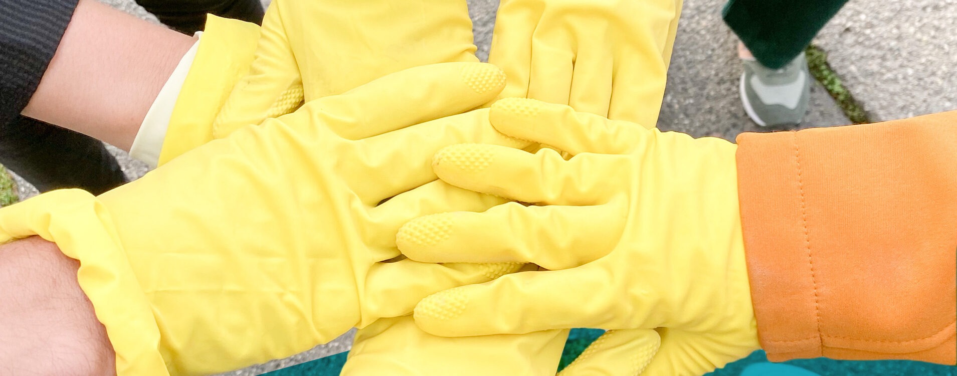 Sechs Hände mit gelben Handschuhen berühren sich in der Mitte zum Gruß