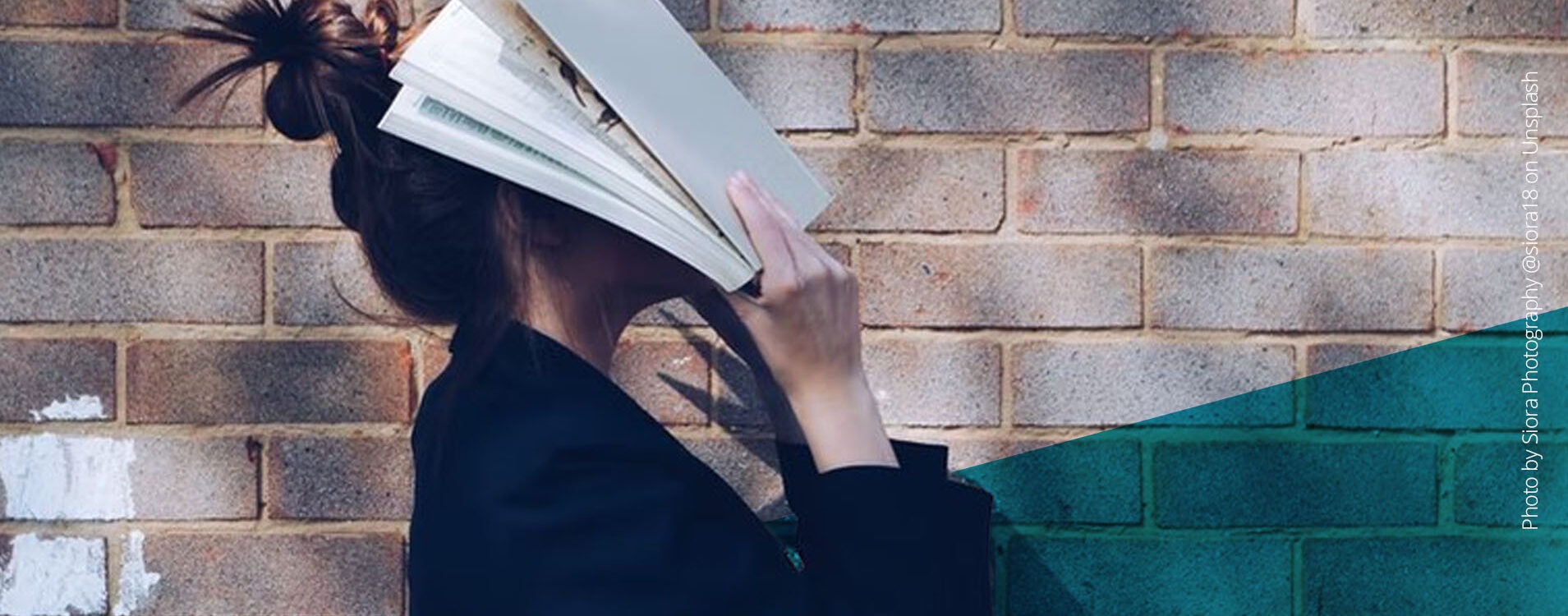 Frau mit braunen Haaren, von der Seite zu sehen, hält sich ein Buch ins Gesicht