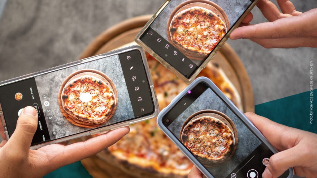 Drei Handys von oben, die ein Bild von einer Pizza machen