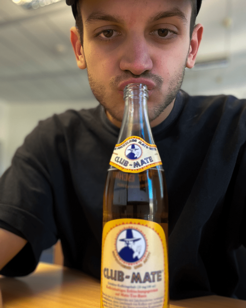 Junger Mann am Schreibtisch mit einer Club Mate Flasche am Mund