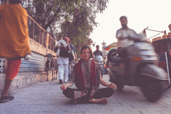 Frau meditiert im Schneidersitz auf der Straße, auf der Leute um sie herumlaufen