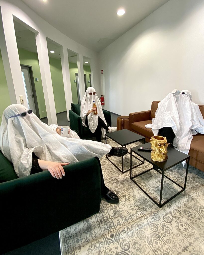 Drei Personen sitzen als Geister verkleidet um einen Tisch