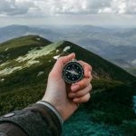 Hand mit Kompass schaut von einem Berg in die Ferne