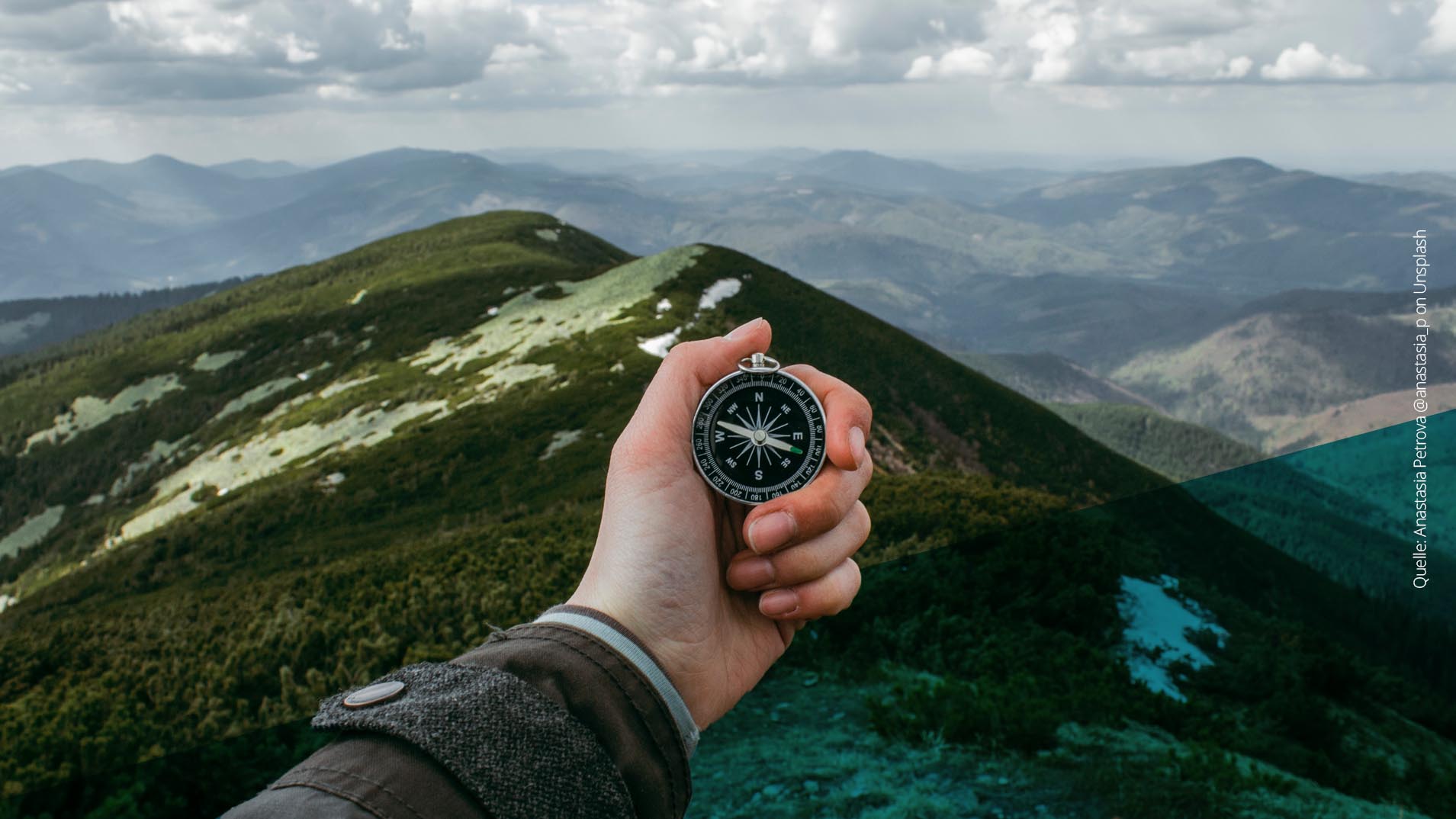 Hand mit Kompass schaut von einem Berg in die Ferne