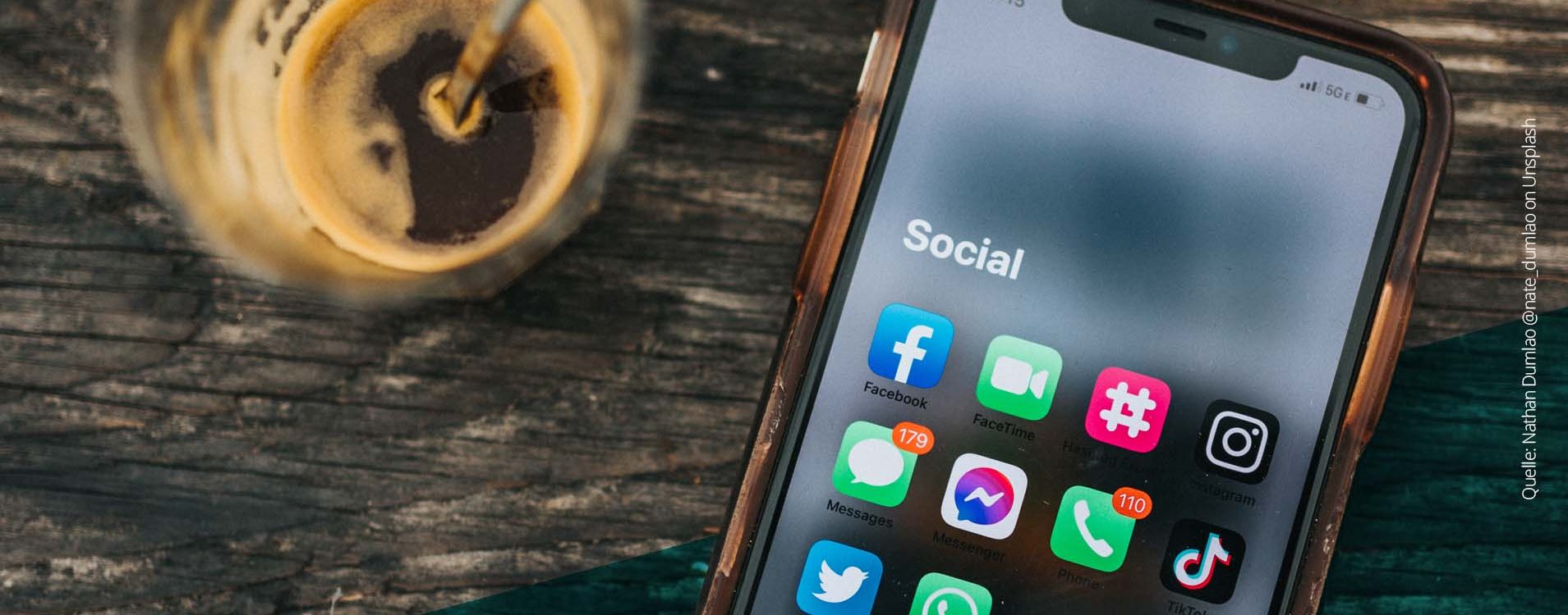 Handy auf einem Tisch mit einigen Social Media Apps auf dem Bildschirm, daneben eine Kaffeetasse