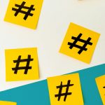Gelbe Klebezettel mit aufgemalten Hashtags verteilt auf einer weißen Wand